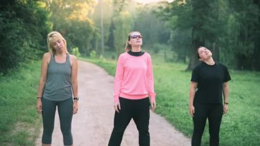 Üç orta yaşlı kadın parkta sabah ısınması yapıyor..