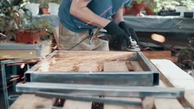 Kaynaklanmış eklemlerin öğütülmesi. Bir adam, metal bir ürünü, bir açı öğütücüyle işliyor. Yakın plan..