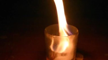 Burning Candle flame inside a glass surrounded by dark background