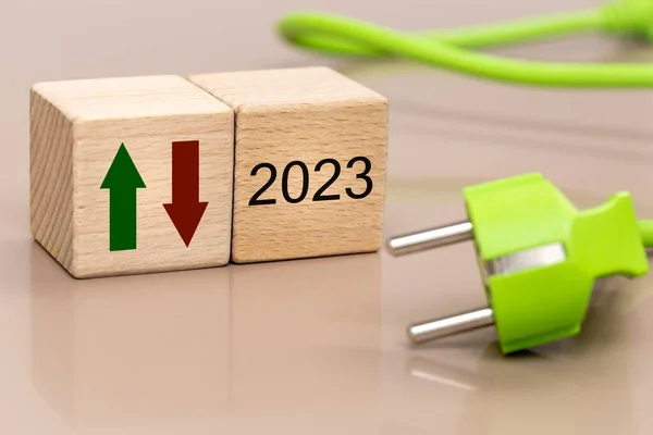 energy prices in 2023, energy crisis concept, rising cost of sourcing raw materials, wooden blocks with date, green and red arrow up and down, green cable with plug