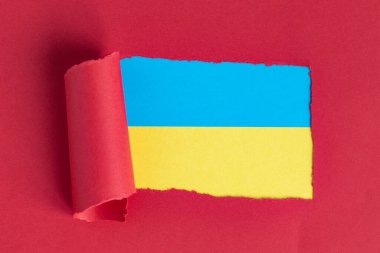 Yırtık kırmızı kağıdın arkasında Ukrayna bayrağının renkleri beliriyor. Boşluğu kopyala