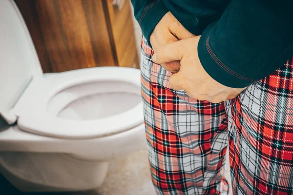 A man in pajamas in the toilet squeezes his crotch and lifts the toilet seat, Urination problem,  Health concept, Male prostate problem, urinary system function, bladder pain