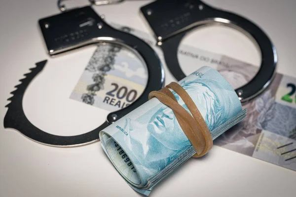 stock image Handcuffs lying on the table next to a bundle of Brazilian money, Concept, Criminal activity in Brazil, Illegal business, Black market