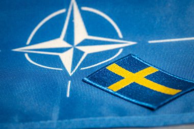 İsveç bayrağı, NATO 'nun, Savunma Örgütü' nün sembolünün arka planına karşı 4 Nisan 'da yeni bir üye ülkeyle ittifak sınırlarını genişletme kavramı. 2023