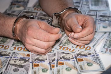 Elleri kelepçeli ve binlerce dolar masaya saçılmış, suç faaliyetleri, tutuklama, yasadışı işler, kapatın.