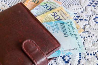 Venezuela parası kahverengi bir cüzdanda, beyaz bir masa örtüsünün üzerinde duruyor, ev bütçesi ve finans konsepti.