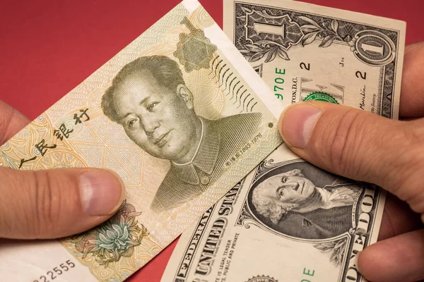 One Chinese yuan and One US dollar banknotes held in hand, Financial concept, Economic and financial competition, Global foreign exchange market, Red background