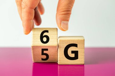 6G sembolü zamanı. El ahşap küpü döndürür ve 5G işaretini 6G olarak değiştirir. Kavram, teknoloji geliştirme, yüksek hızlı iletişim ağı ve 6G. Güzel fuşya ve beyaz arkaplan