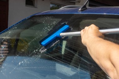 Bir adam istasyondaki arabanın ön camını yıkıyor, yolda görüş mesafesini arttırıyor, sürücü güvenliğini arttırıyor.