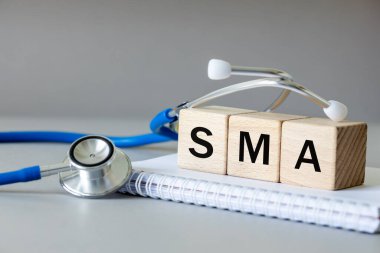 Beyaz defter, tıbbi steteskop ve tıbbi kısaltması SMA olan tahta bloklar omurilik kasları körelmesi, ağır genetik hastalıklar, güzel gri arka plan, tıbbi konsept.