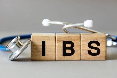 Tıbbi steteskop ve üzerinde IBS yazan tahta bloklar, asabi bağırsak sendromunun kısaltması, fonksiyonel doğanın kronik bir hastalığı, gri arka plan.