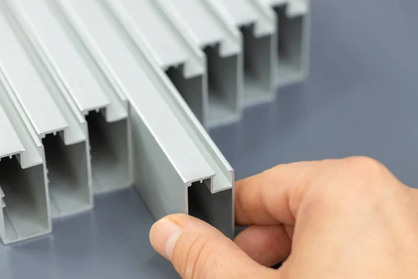 stock image Aluminum profiles on a gray background, a hand extending an aluminum component, a material used in the construction industry, lightweight aluminum structures, interior finishes, doors and frames, raw material price increase