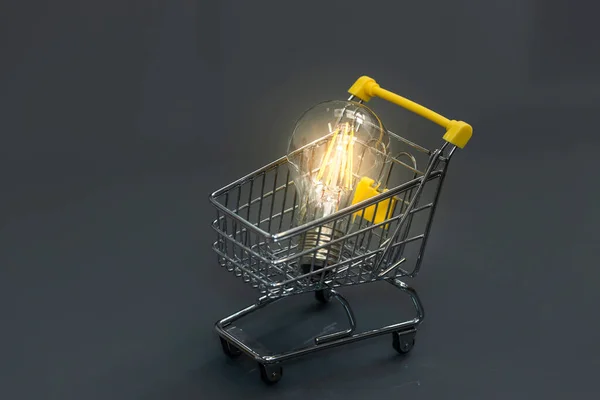 Glowing light bulb in shopping cart on dark gray background, Creative light bulb idea, power energy or business idea concept