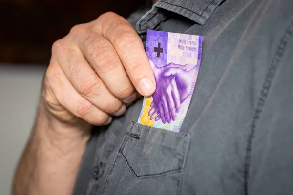 The man takes a thousand Swiss francs out of his shirt\'s pocket, the highest denomination of paper money in Switzerland, business concept, 1000 francs banknote