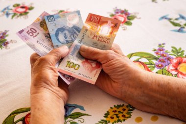 Meksika parası, Eldelry kadını elinde birkaç Meksika pesosu, emeklilerin mali sorunları, düşük emekli maaşları, yüksek fiyatlar.