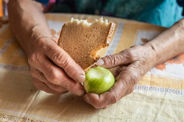 Poverty of old and lonely people, Social assistance concept, old woman holds dry slice of bread and raw onions in her hand, financial situation of pensioners,deprivation,basic problems in life