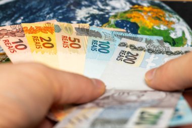 Brezilya parası, Brezilya reais 'i dünya haritasında tutan eller, finansal iş konsepti, dünya para birimi, küresel ekonomi