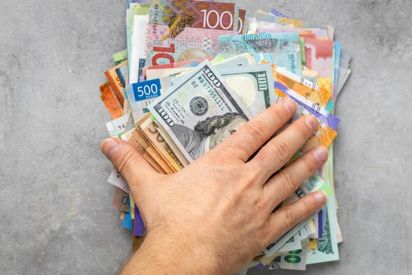 hand placed on a pile of money from all over the world. Financial concept, currency markets, money exchange, beautiful gray background, copy space