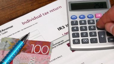 Yeni Zelanda 'da yıllık vergi iadesi, konsept, ofis vergisi, vergi formu, adam hesap makinesinin vergisini hesaplar, para yığını Yeni Zelanda doları