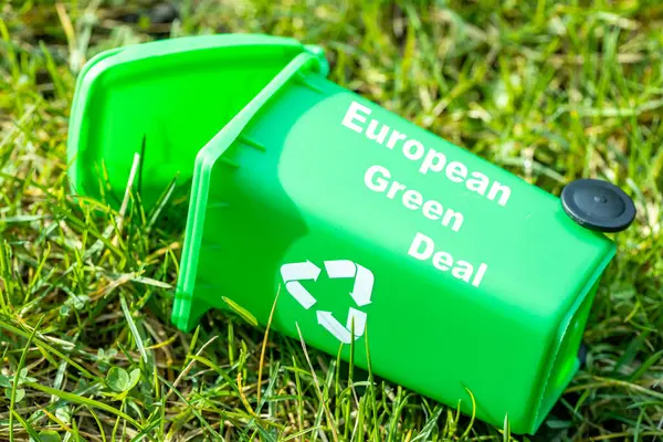 green garbage bin lying in the grass with the text European Green Deal, Environmental concept, Changes in the Green Deal, Farmers\' protests, ecological project, close up