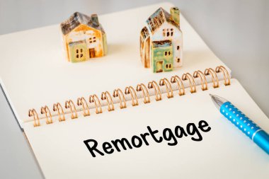 Remortgage - a word written in a notebook with a pen and a ceramic miniature of a house. Business and financial concept, copy space clipart