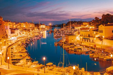 Menorca adasındaki tarihi turizm kasabası Ciutadella. Limanın ve körfezin gece manzarası, Eski Şehir ve suda sallanan tekneler.