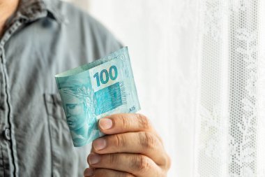 Brezilya parası, bir adam elinde 100 Brezilya Reais banknotu tutuyor. Finansal iş kavramı