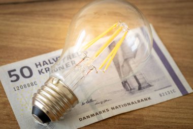 Danimarka parasının üzerinde parlayan ampul, kavram, elektrik zamları, Danimarka ev finansmanı