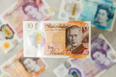 İngiltere Merkez Bankası tarafından Haziran 2024 'te çıkarılan King Charles III ile Yeni Britanya Para Birimi. Arka planda, Kraliçe 'nin görüntüsüne sahip eski banknotlar var.