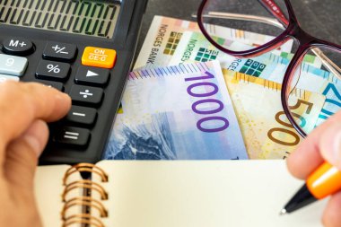 Norveç Krone, finansal analiz, şirket muhasebesi, vergi hesaplaması, finans sektörü konsepti. Norveç parası ve hesap makinesi. Sonuçları bir deftere el yazısıyla yazmak.