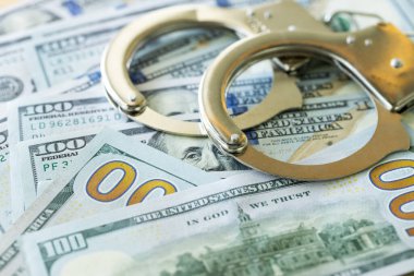 Handcuffs and a lot of dollars scattered on the table, concept of financial abuse, Money embezzlement, Illegal trade, Profiting from criminal activity. clipart