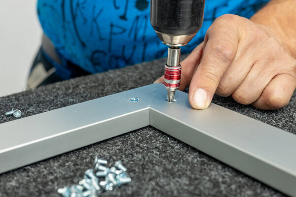 Рабочий вручную собирает алюминиевые рамы