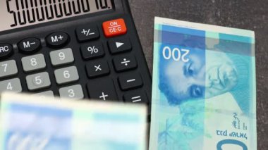 İsrail şekelleri ve hesap makinesi. Hesap makinesinin yanındaki masaya hesap makinesiyle para sayıp yaymak. İsrail parası. Finansal konsept, kapat