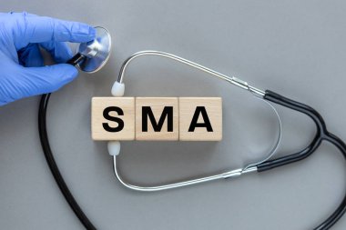 Spinal kas atrofisi SMA, doktorun elindeki tıbbi steteskop ve tahta bloklar üzerindeki kısaltma, gri arka plan, tıbbi konsept, hastalık varlığı, kopyalama alanı