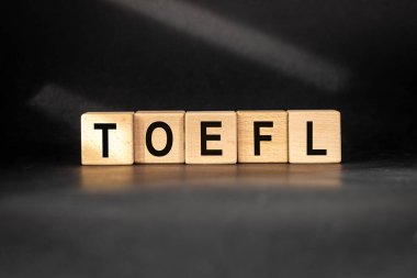 Tahta bloklara yazılmış TOEFL (Yabancı Dil olarak İngilizce Testi) Kavramsal slogan. Güzel siyah arkaplan, doğal olarak aydınlık.