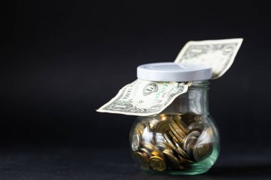 Bozuk paralarla dolu kavanoz ve bir dolarlık banknot. Finansal iş konsepti, finansal eğitim, tasarruf ve artan sermaye, kopyalama alanı. Güzel siyah iş geçmişi