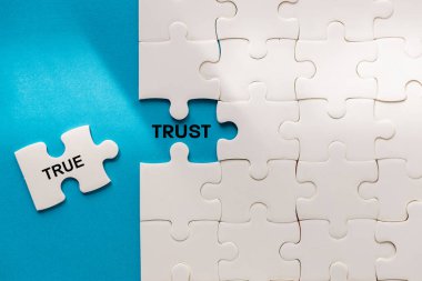 Symbol of true trust. The word TRUE from the puzzle reveals TRUST. Business concept. Truth and honesty builds trust. Blue background, copy space clipart