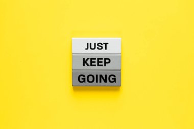 Sadece devam et. Ahşap bloklardaki slogan. Motive edici kelimeler, şirket desteği, insanları yönetmek için modern yöntemler. Sarı arka plan. Boşluğu kopyala