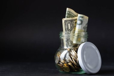 Bozuk paralar, küçük avrolar ve dolar banknotları olan kavanoz. Finansal iş konsepti, finansal eğitim, tasarruf ve artan sermaye, kopyalama alanı. Güzel siyah iş geçmişi