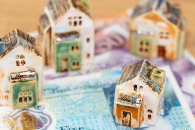 Tahta bir masa üzerinde banknotları olan minyatür ev modeli, ev kredisi konsepti, İngiliz sterlini ve İngiltere emlak piyasası