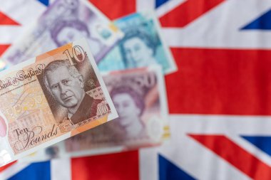 İngiltere Merkez Bankası tarafından Haziran 2024 'te çıkarılan King Charles III ile Yeni Britanya Para Birimi. Arka planda, Bayrak ve Kraliçe 'nin resmine sahip eski banknotlar