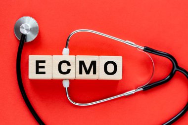 ECMO ya da Extracorporeal Membrane Oxygenation technique of exorporeal blood oxygenation. Tıbbi konsept. Tıbbi steteskop, ahşap küplere yazılan kısaltma, kırmızı arkaplan, kopyalama alanı