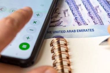 Birleşik Arap Emirlikleri parası. Akıllı telefon hesap makinesine, AED sembolüne ve defterdeki notlara güvenerek. Finansal anlaşma, ev bütçesi, BAE döviz kuru, şirketin mali analizi