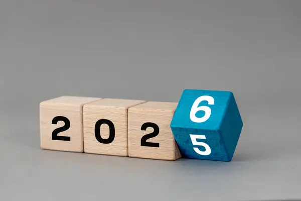 2026 yılı. Yıl 2025 'i 2026 olarak değiştir. Tahta bloklar ve tarihi değişmiş. Gri arka plan. İş hayatında yeni yılı simgeliyor. Yakın çekim