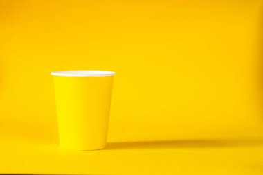 Sarı arka planda sarı kağıt bardak. Boşluğu kopyala