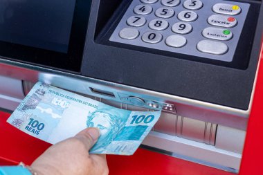 Brezilya parası. Bir kadın ATM 'den 100 Brezilya banknotunu çekiyor. Mali konsept. 