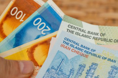 İsrail ve İran 'ın parası. İş ve finansal konsept. İsrail şekelleri ve İran ritüelleri ellerinde. Karşılıklı ilişkiler ve bunun her iki ülkenin para birimi üzerindeki etkisi. Kapat.