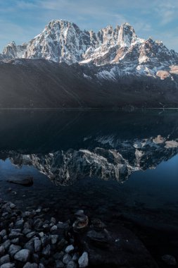 Bu dikey bir görüntü, karla kaplı bir dağ ve onun yansıması Gokyo Gölü denen durgun su gölünde. Himalayalar 'ın derinliklerinde, Nepal sınırında bulunan sakin Gokyo köyü, gölün etrafında kurulmuştur..