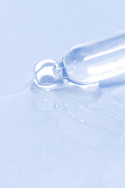 Cosmetic pipette with dripping liquid and drops on a blue background, serum, serum, gel, vitamin, water, oil. Clean, fresh, moisturizing