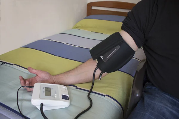 Young person taking blood pressure on top of bed sitting in a chair with a colored bedspread